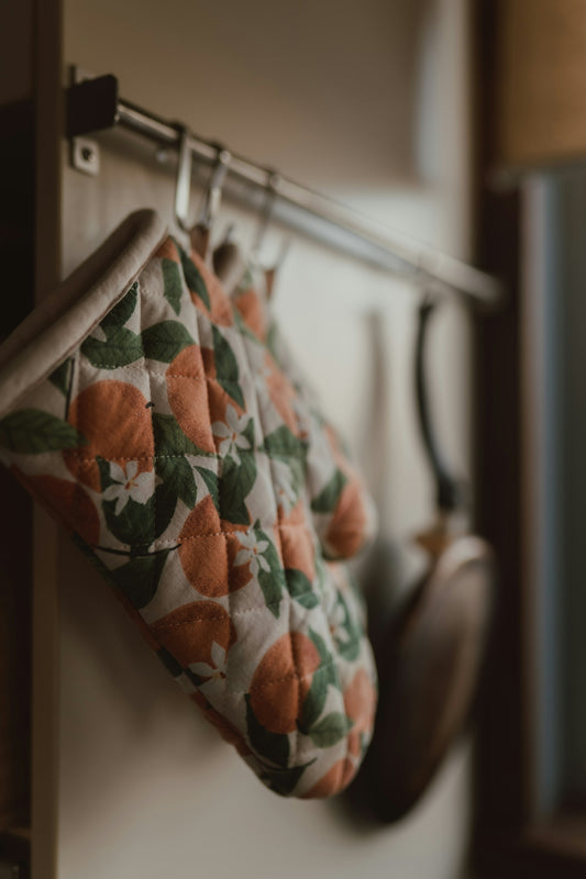 Patterned oven mitt and frying pan hanging in a kitchen.